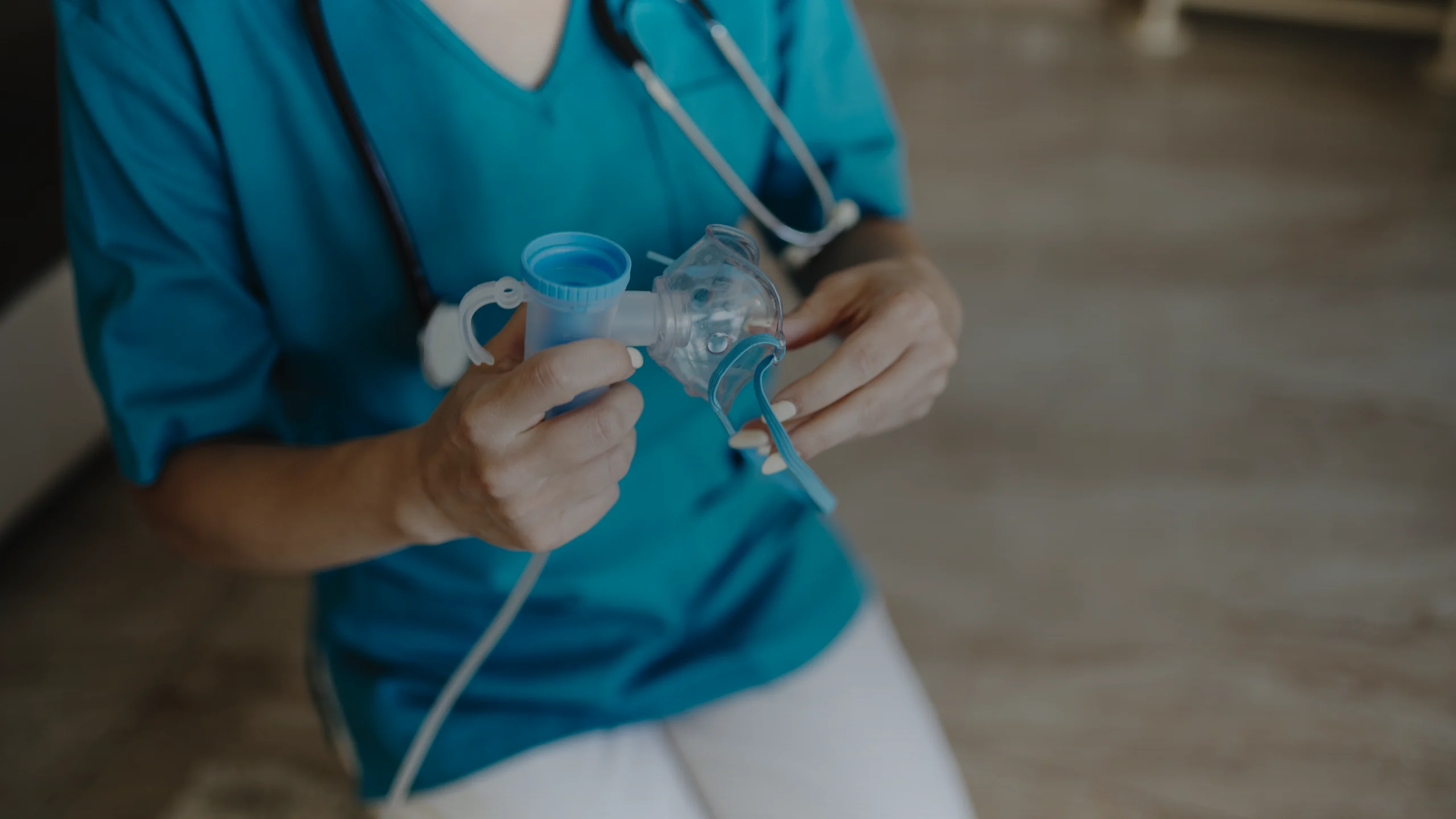 Cuve et masque d'un nébuliseur tenus entre les mains d'une soignante en blouse bleue